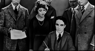 Chaplin sentado e assinando o documento da fundação da United Artists - Wikimedia Commons